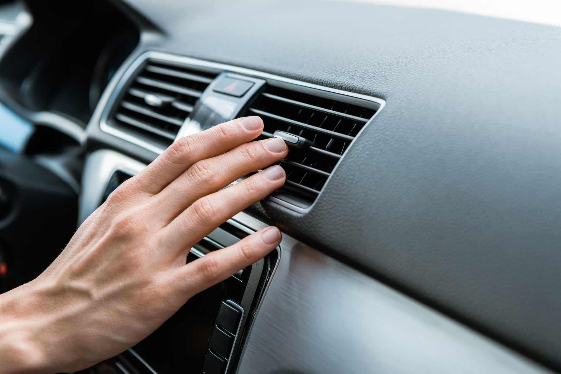 Hand adjusting the car’s dashboard air vent with black and silver interior details