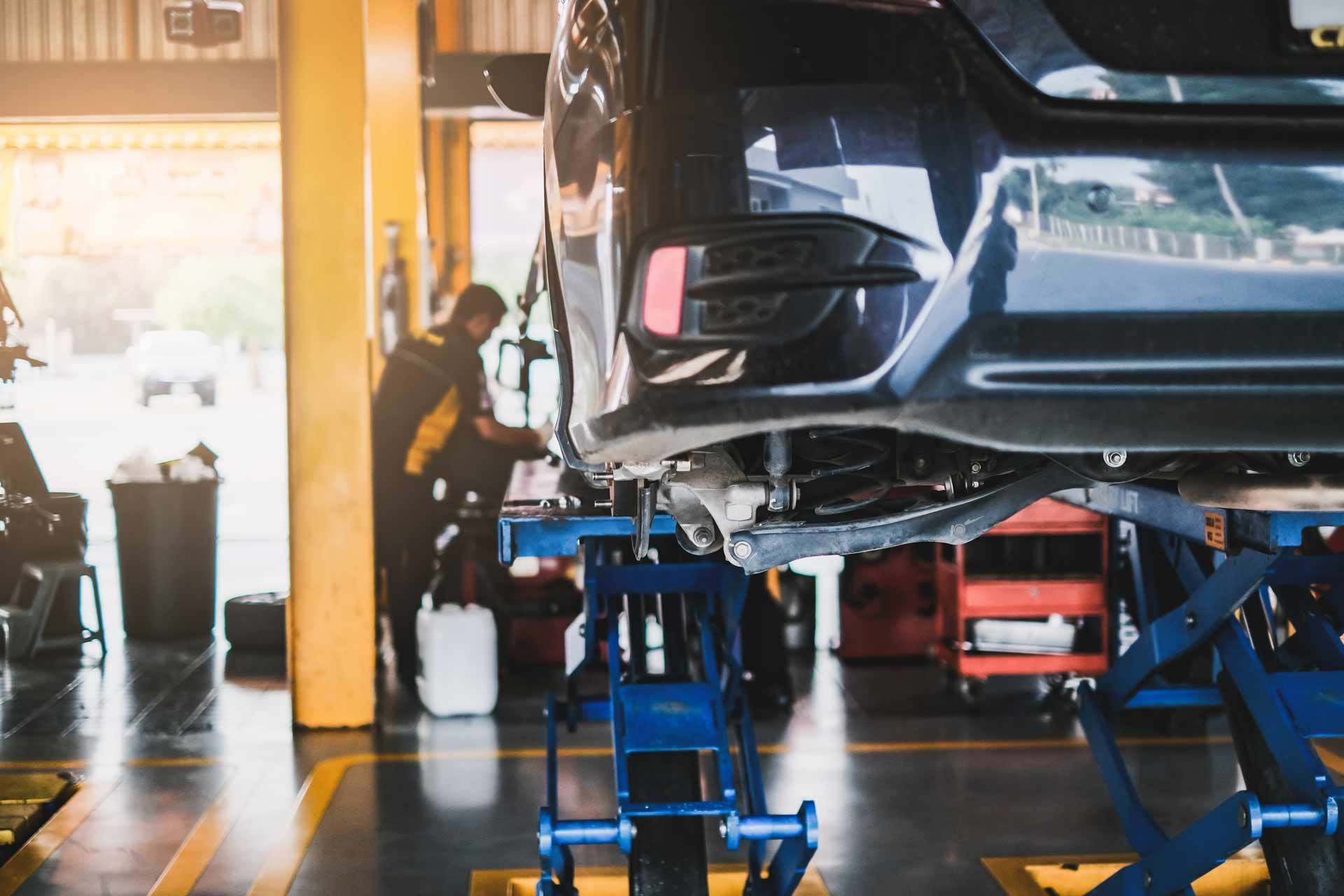 Car on a lift in an auto repair shop, with a mechanic working nearby.