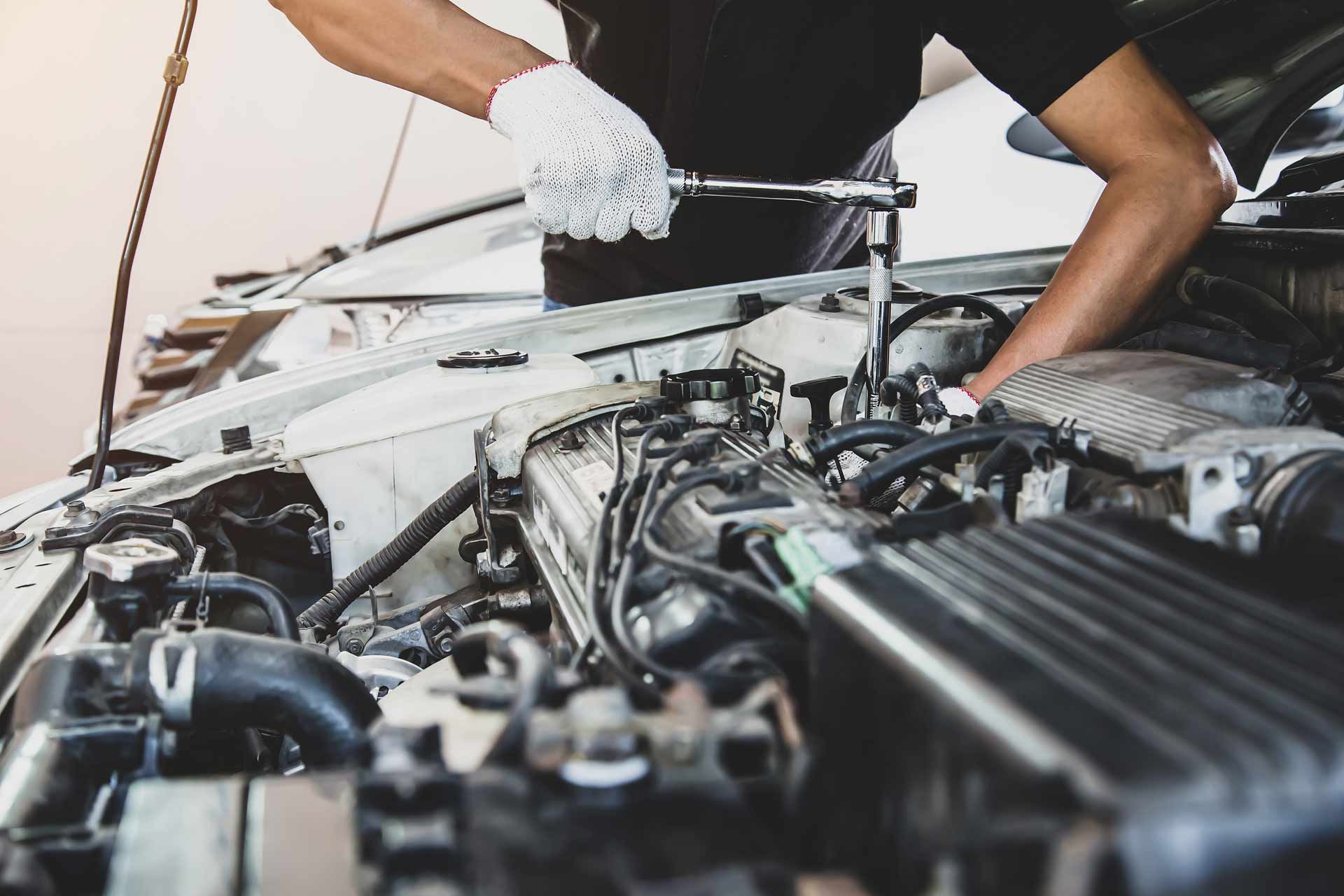 Mechanic working under a car hood with tools in an auto repair shop