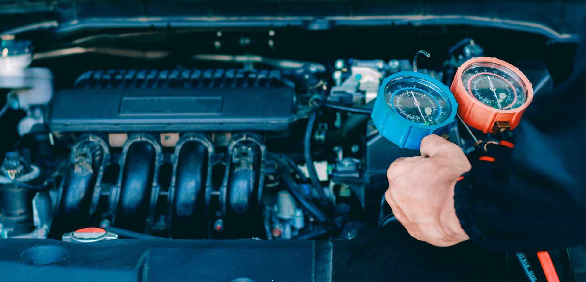 Person holding blue and orange gauges near a car engine