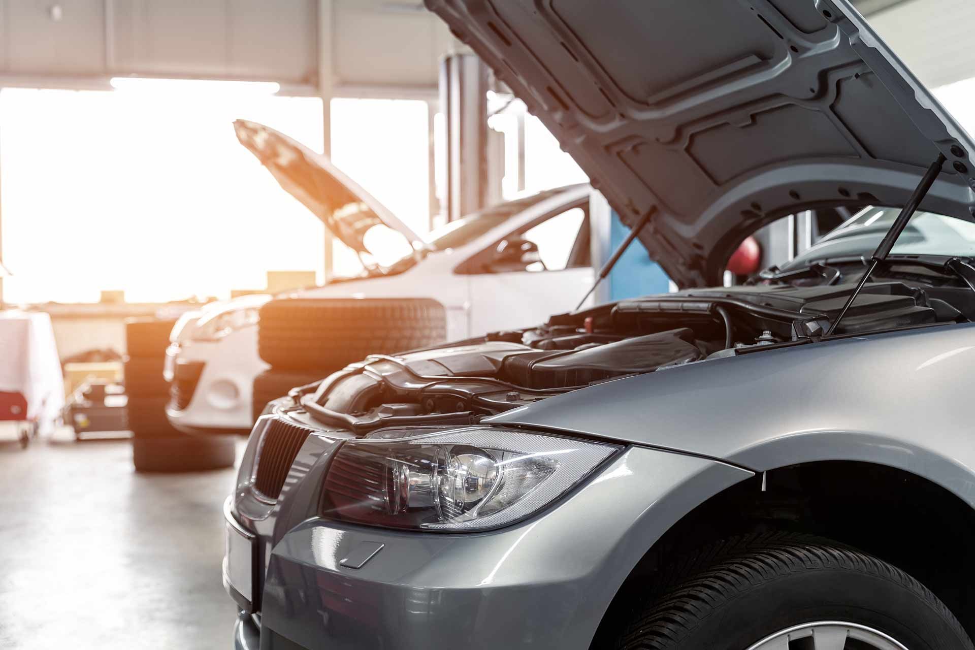 Cars in a bright auto repair garage with one hood open and a mechanic in the background