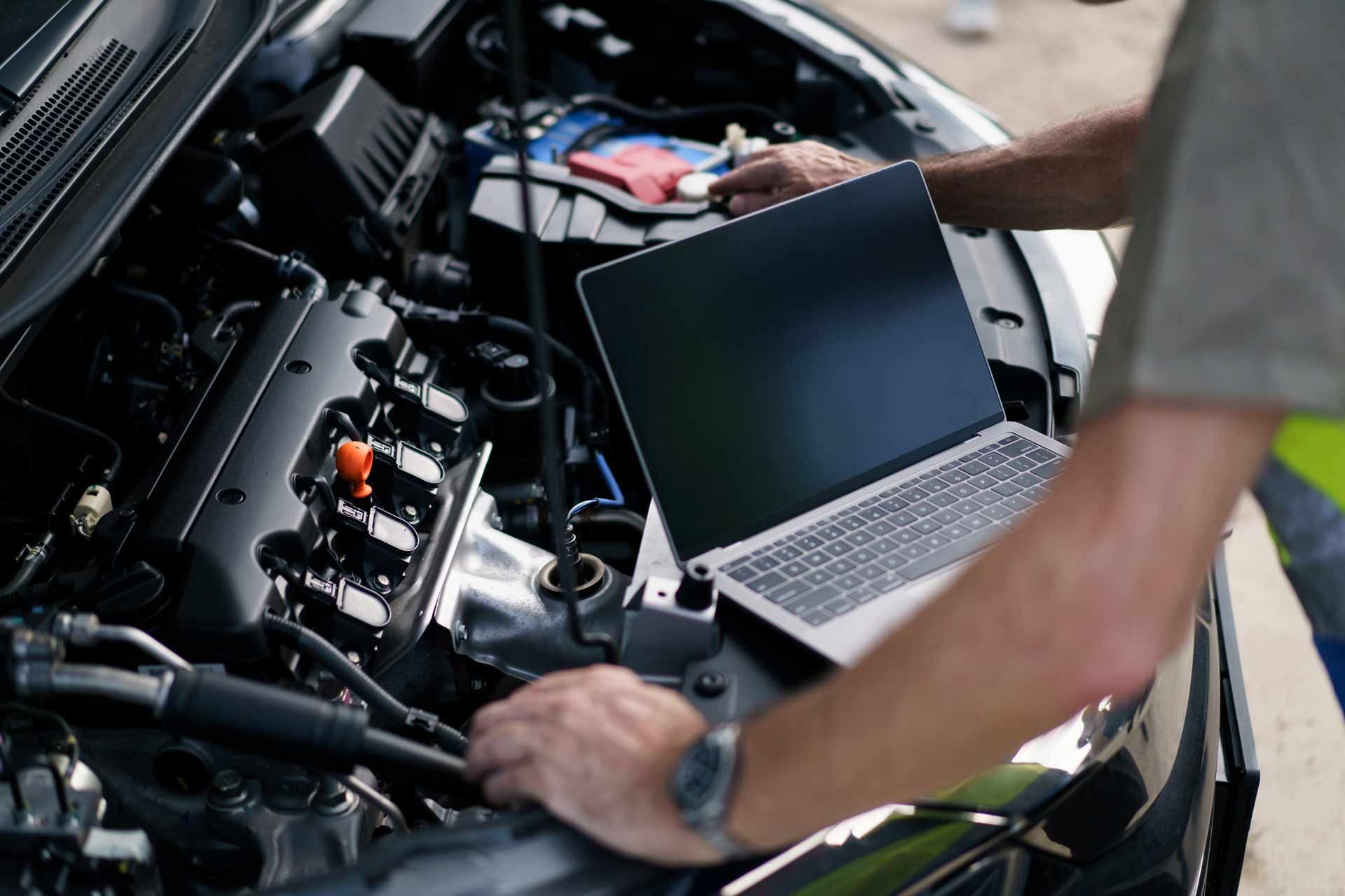 Mechanic inspecting a car engine with a laptop in the open hood area