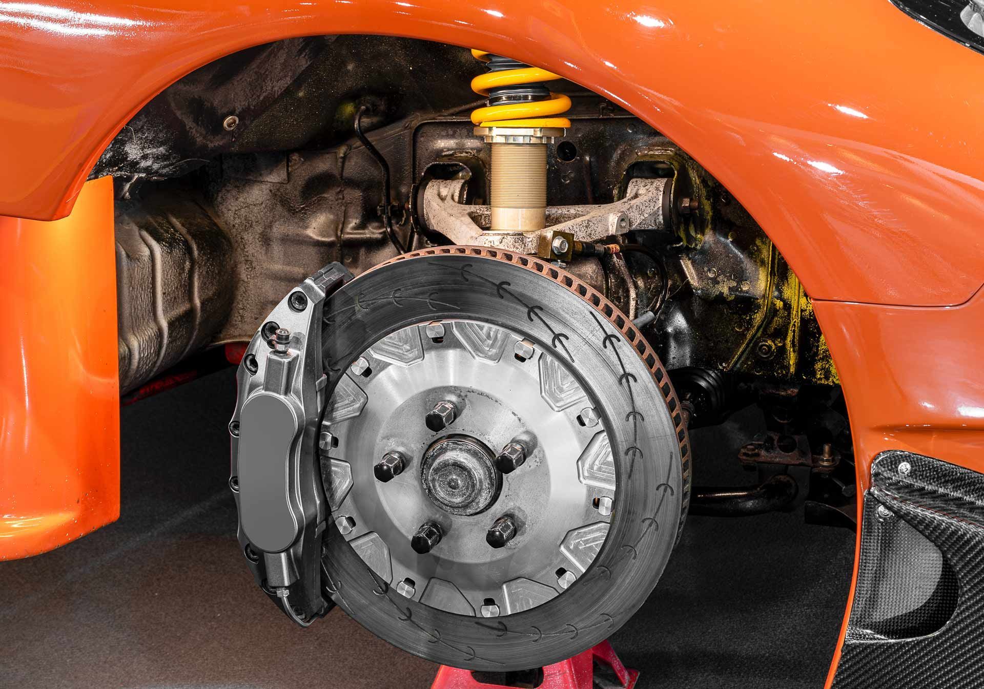 Close-up of a car's front brake assembly and suspension behind an orange fender.