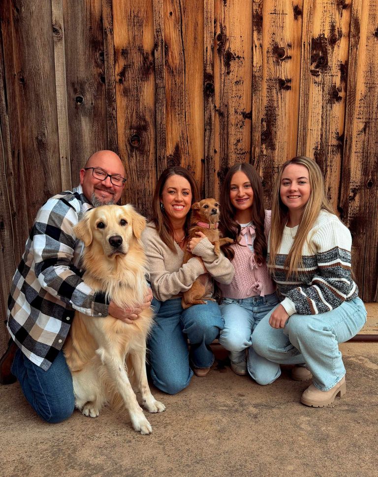 Family posing with a golden retriever in front of a wooden wall, smiling and crouching together Family posing with a golden retriever in front of a wooden wall, smiling and crouching together