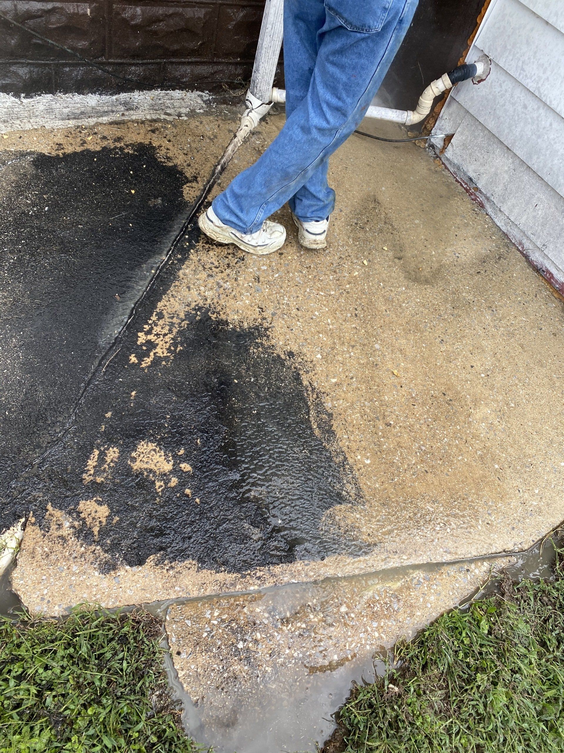 Person standing on cracked, patched concrete beside a doorway and grass