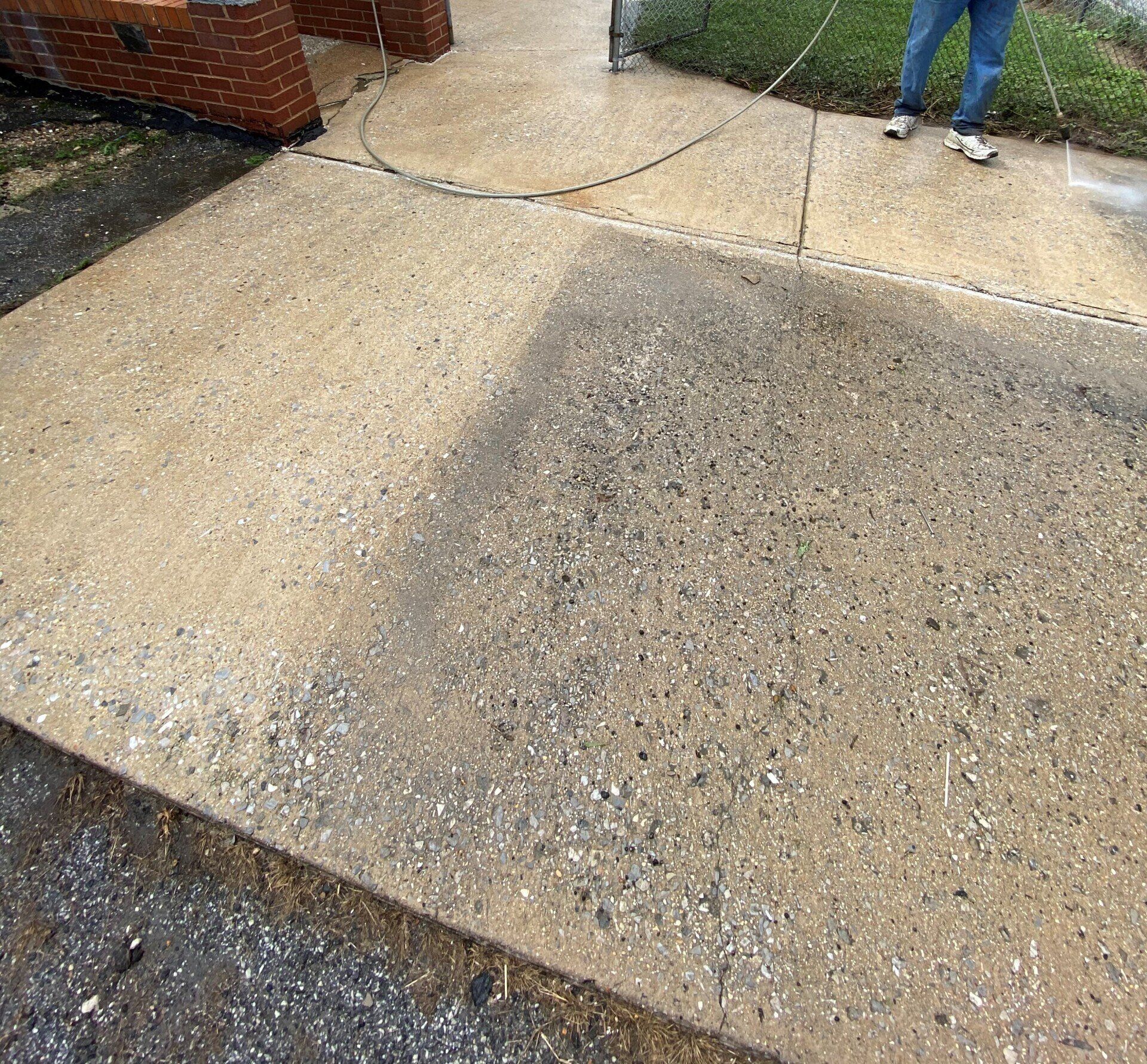 Concrete driveway with a large cracked, resurfaced section near a brick house and a person standing at the top.