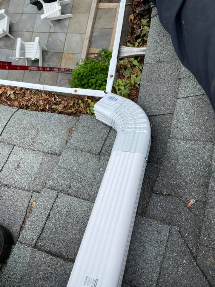 White downspout elbow on gray shingle roof beside gutter and skylight trim