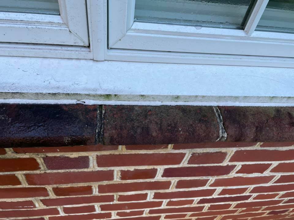 White window frame above a red brick wall with a dark stone sill and worn mortar seam