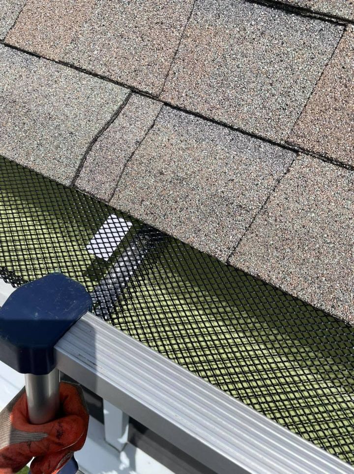 Roof shingles over green mesh and a white railing with a blue-capped post below