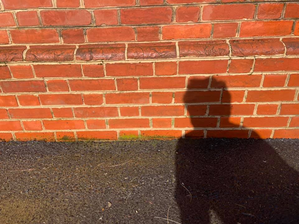 Shadow of a person on a red brick wall beside dark pavement under sunlight
