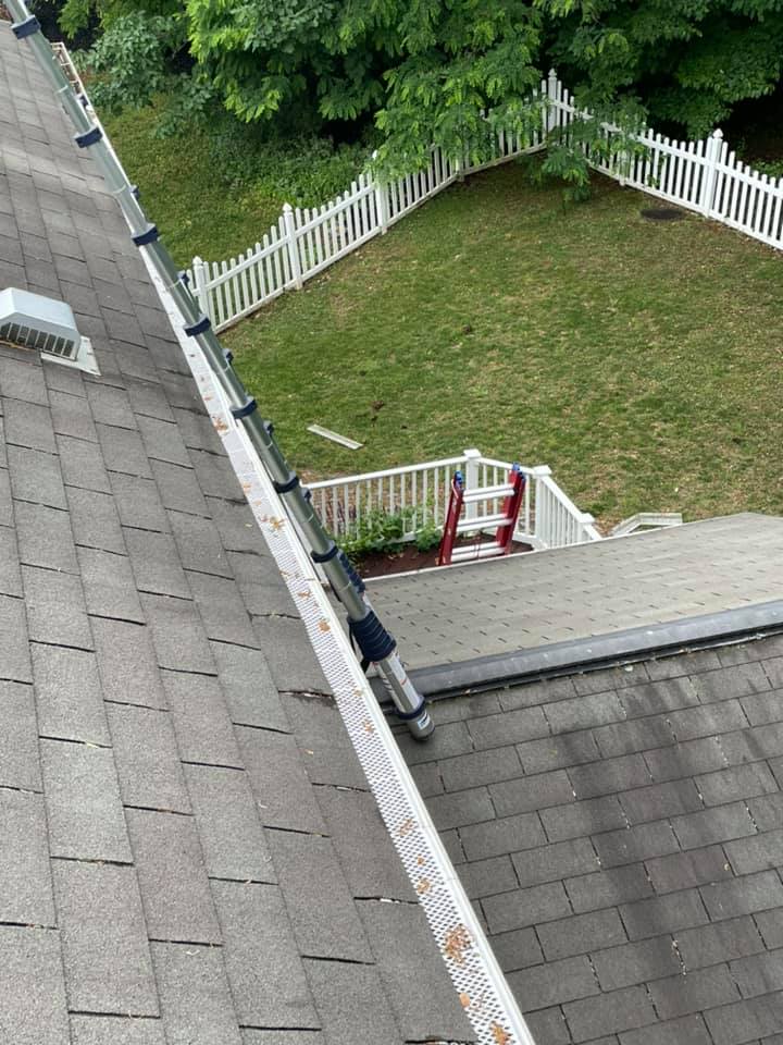 Rooftop view of a small fenced backyard with green grass, trees, and a red gate below.