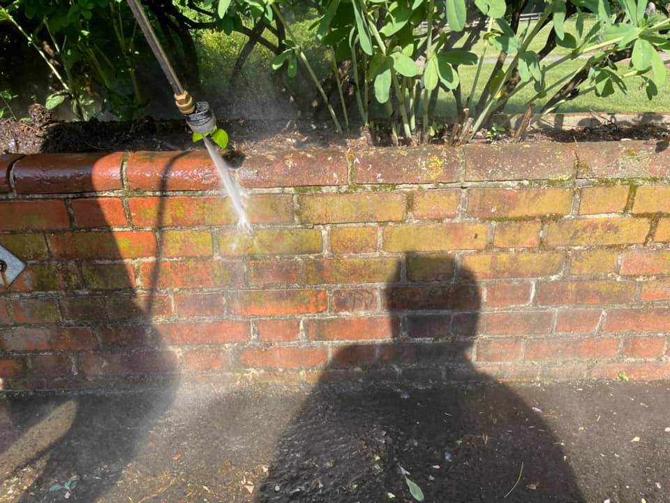 Garden hose spraying water onto a brick wall and pavement, with two shadows in the foreground.