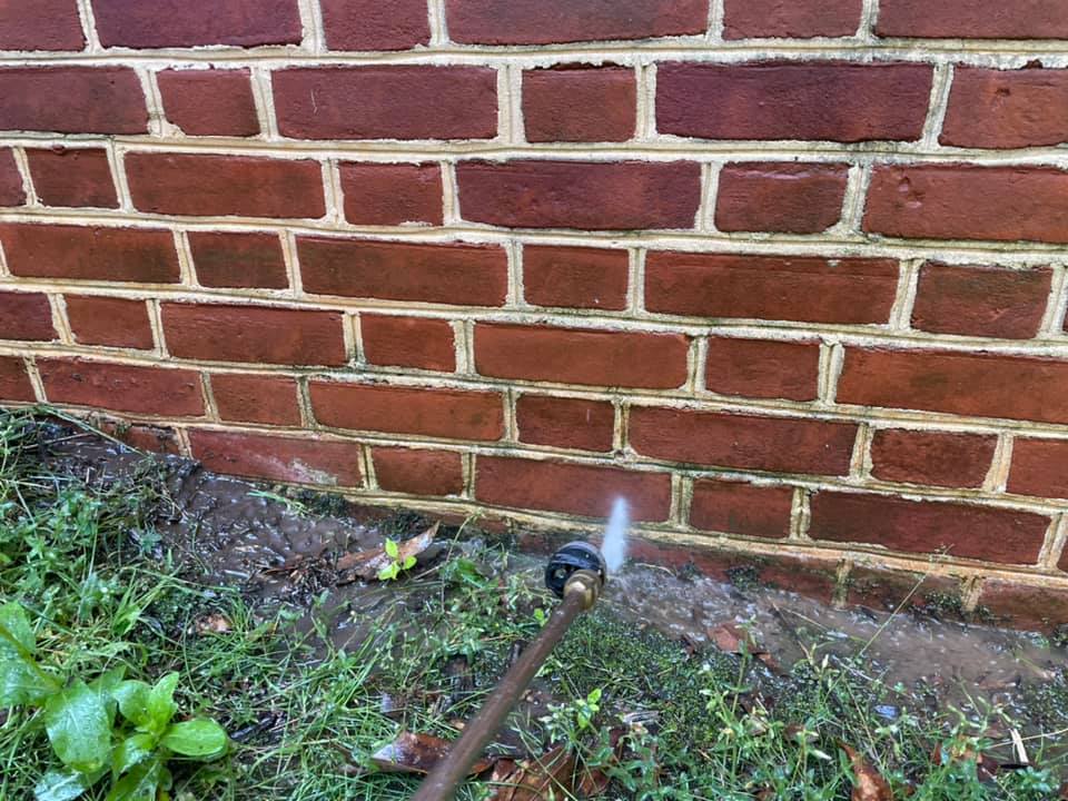 Garden hose spraying water against a red brick wall near the ground