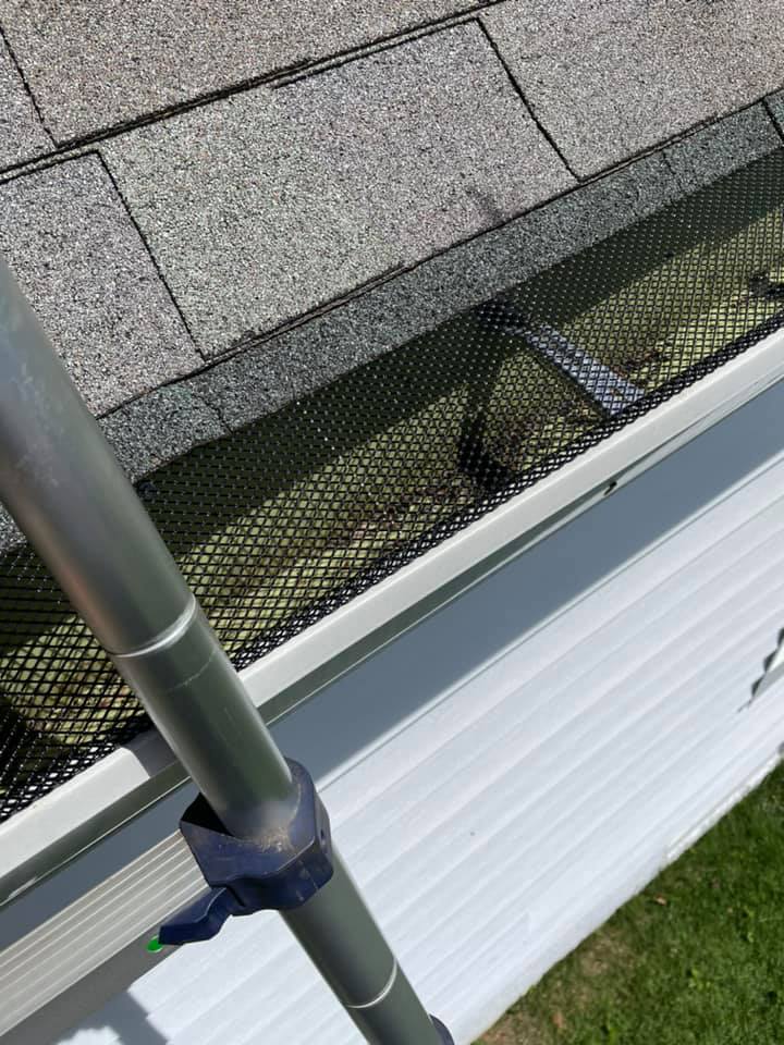 Metal pipe secured with a clamp beside a white gutter and gray roof shingles.