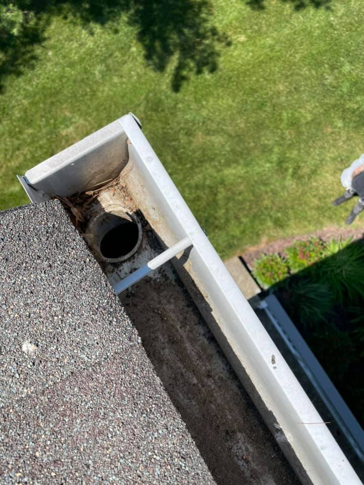 Roof gutter drain opening with gravel shingles, white trim, and green lawn below