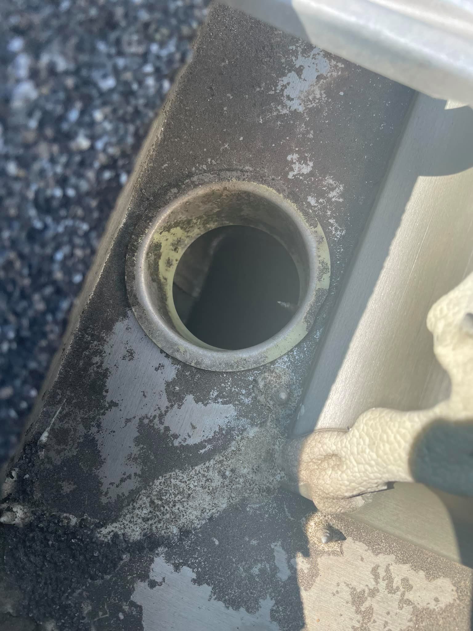 Close-up of a weathered metal tube opening with rust and peeling paint on a textured surface.
