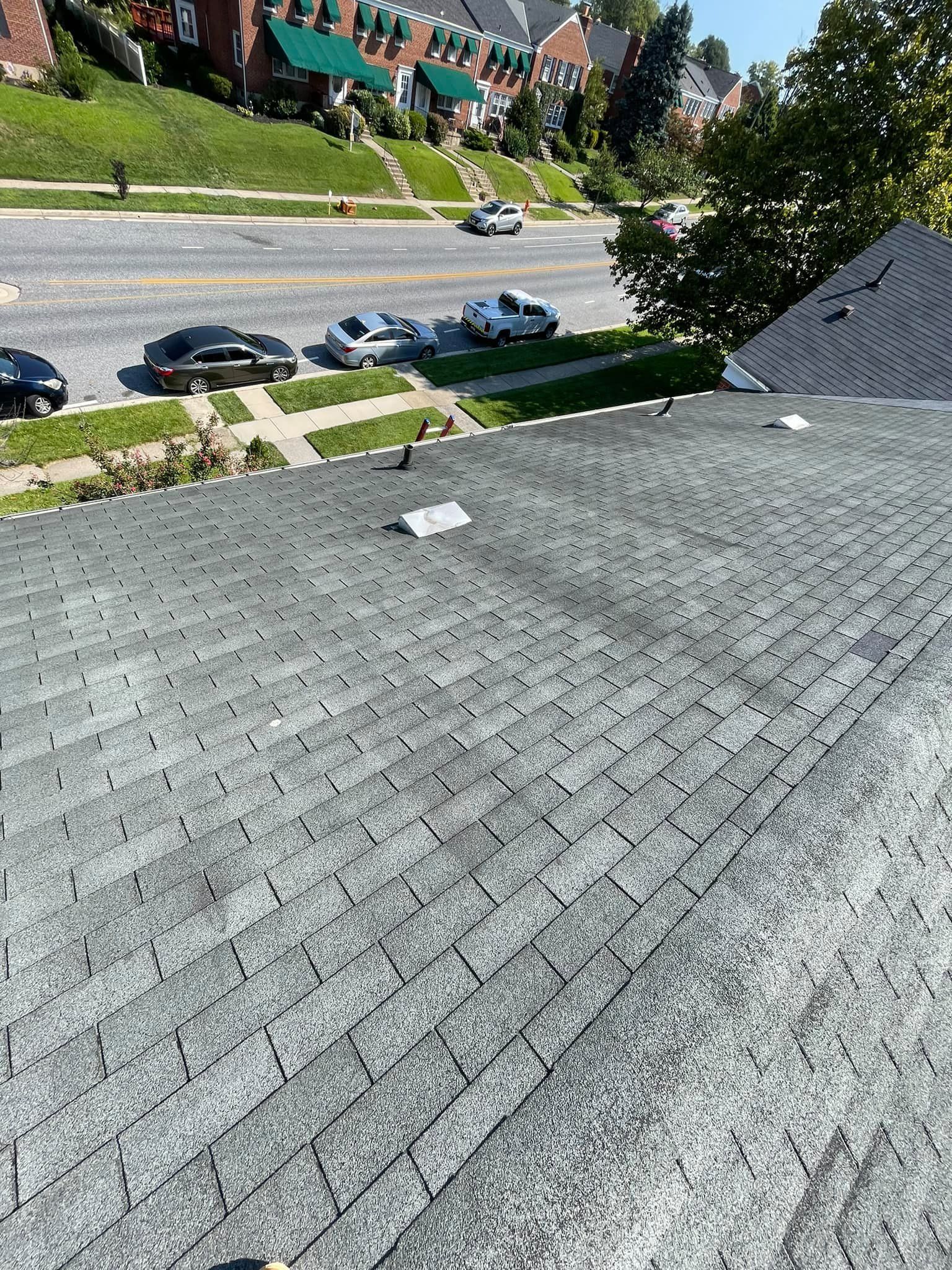Steep gray shingled roof overlooking a street with parked cars and townhouses below