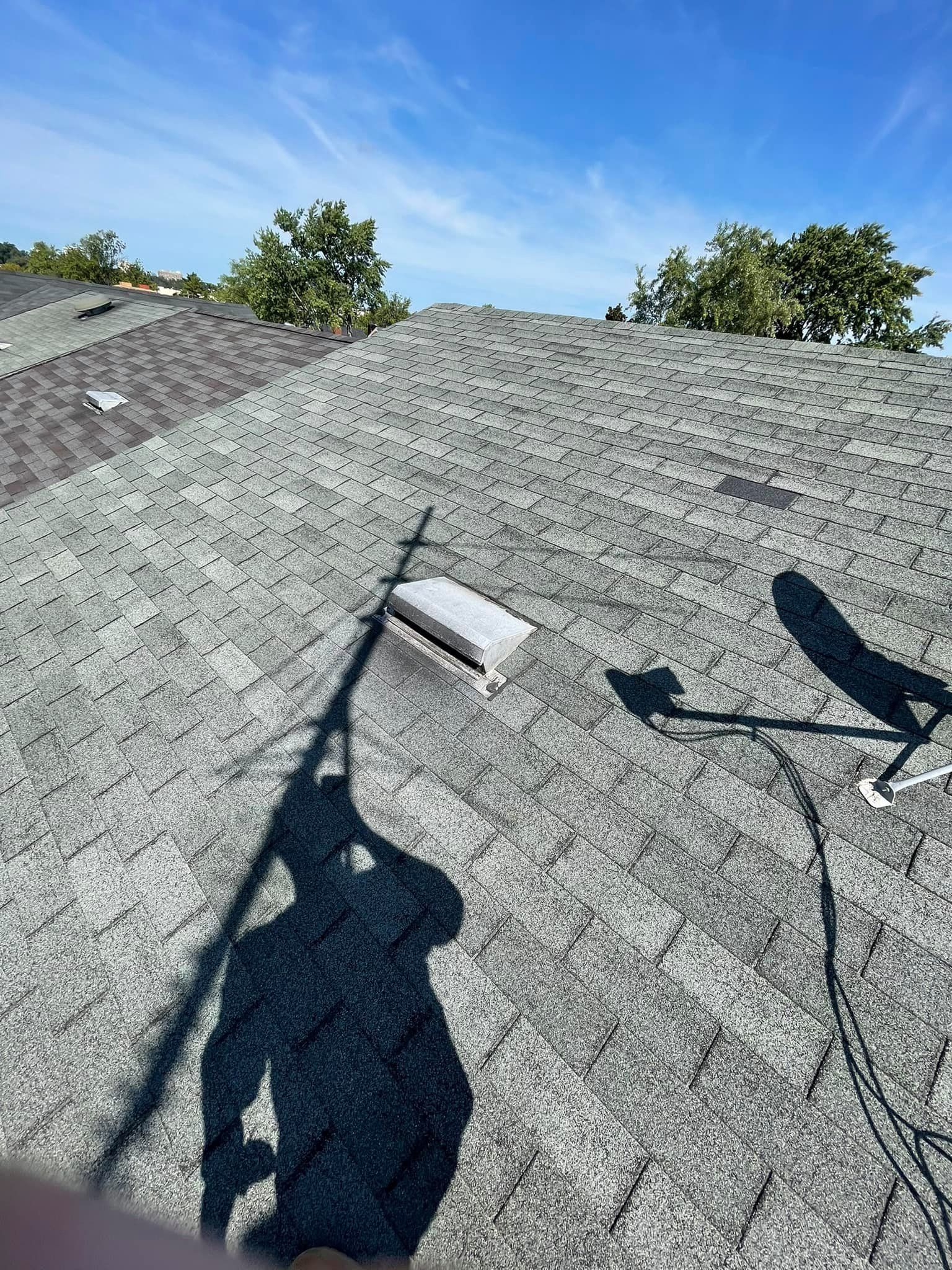 Solar roof with a gray shingled surface, rooftop vent, and satellite dish under a clear blue sky.
