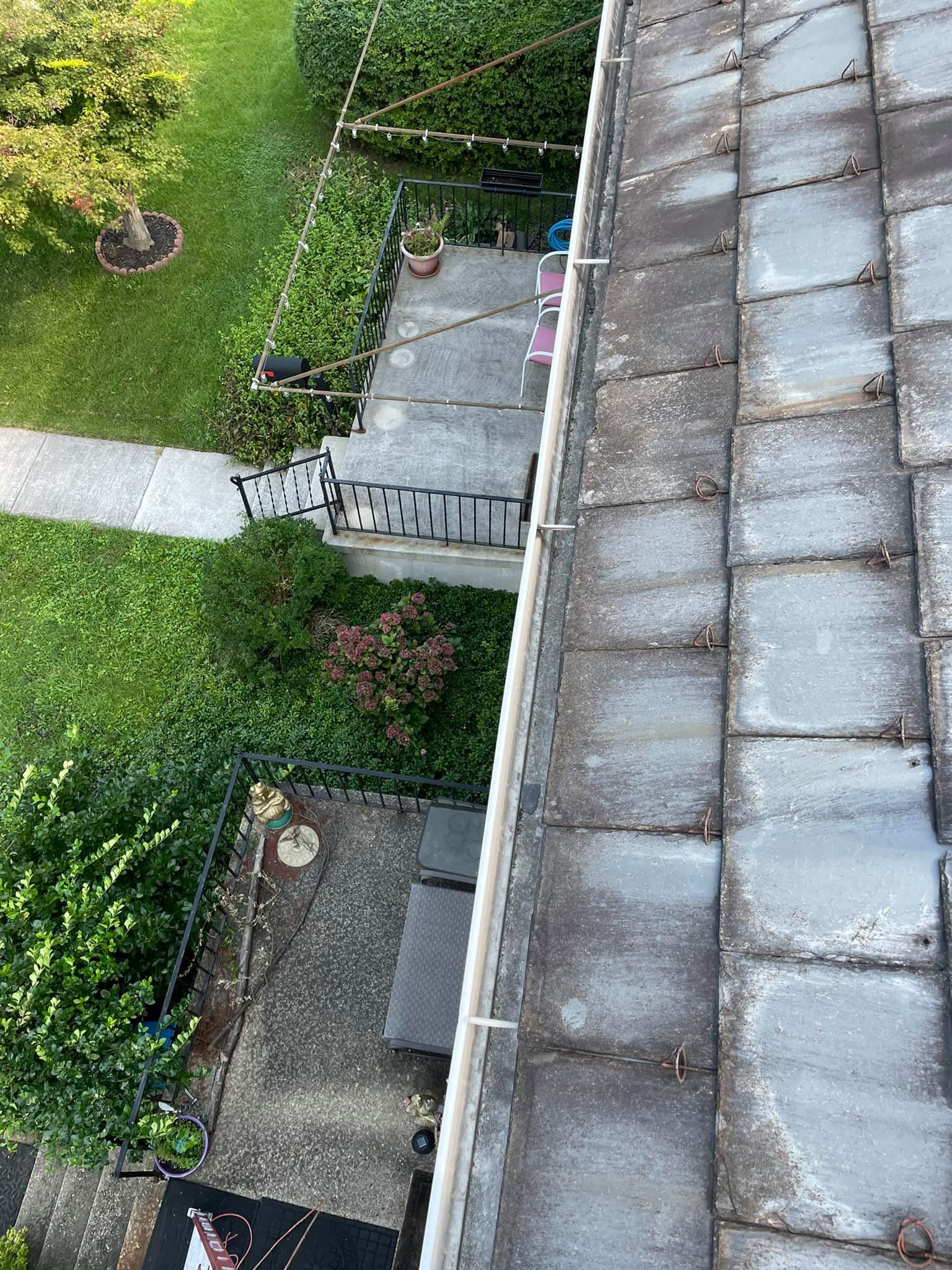 Rooftop view of a backyard with a stone patio, grass, and a narrow path beside a house.