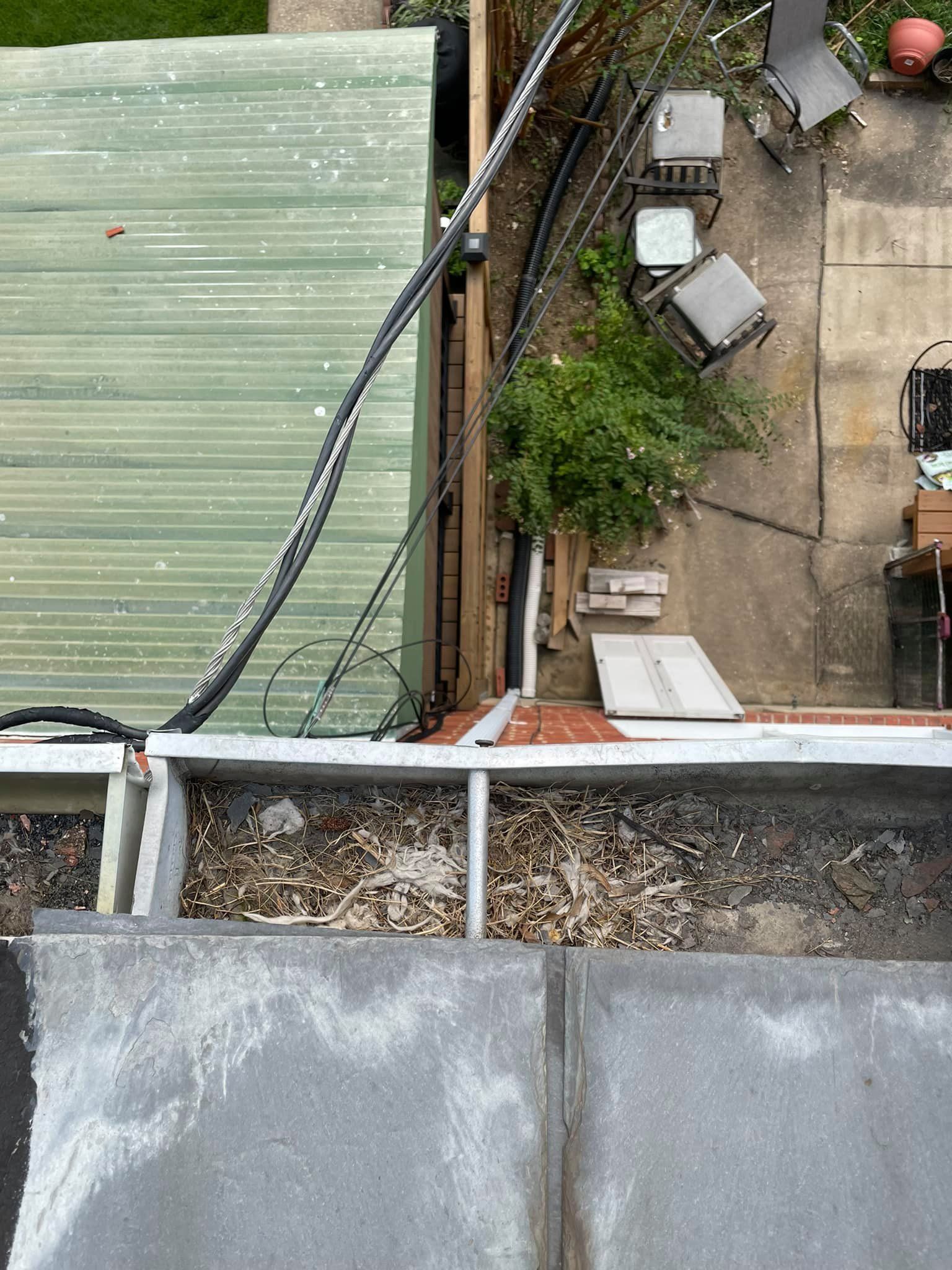 Overhead view of a rooftop edge beside a small backyard with a tree, patio chairs, and sheds