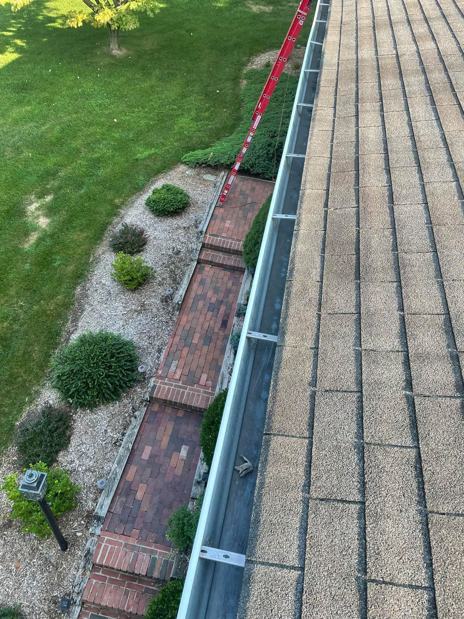 Roof gutter beside brick walkway, gravel border, and green lawn with trimmed shrubs