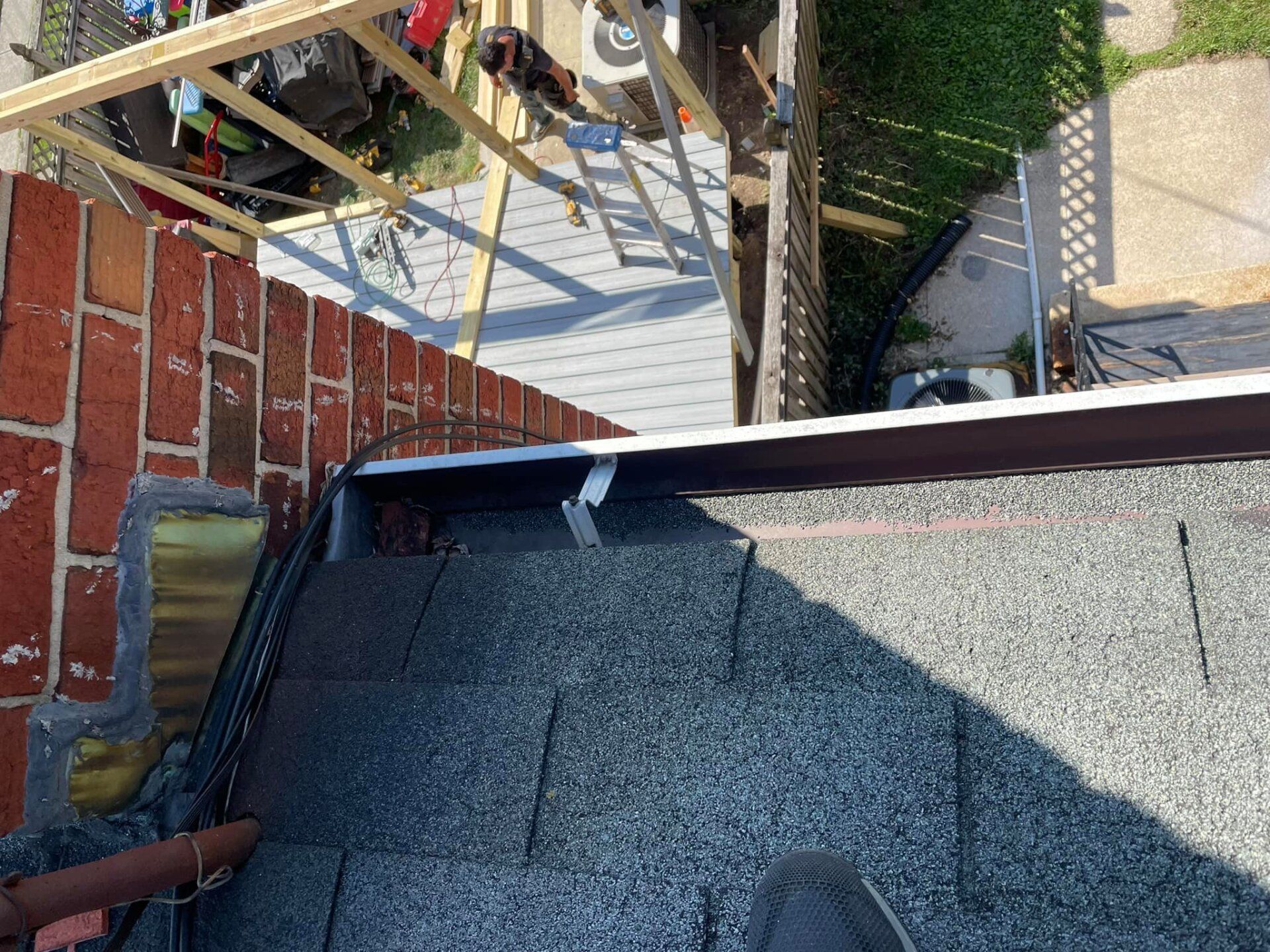 Rooftop edge with gray shingles beside a brick wall and shadowed outdoor walkway below
