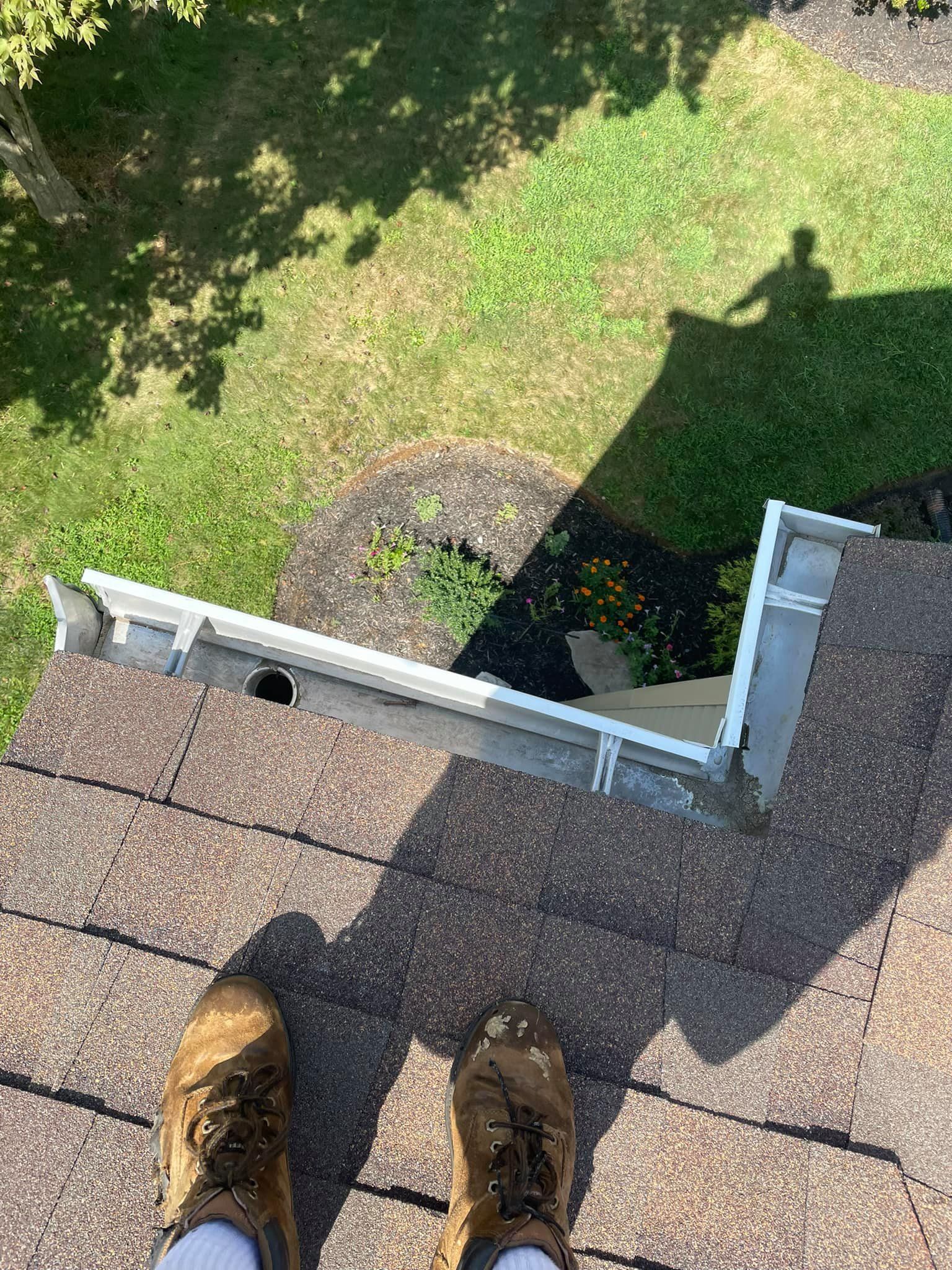 View from a roof edge with boots visible, looking down at a grassy yard and shadow below.