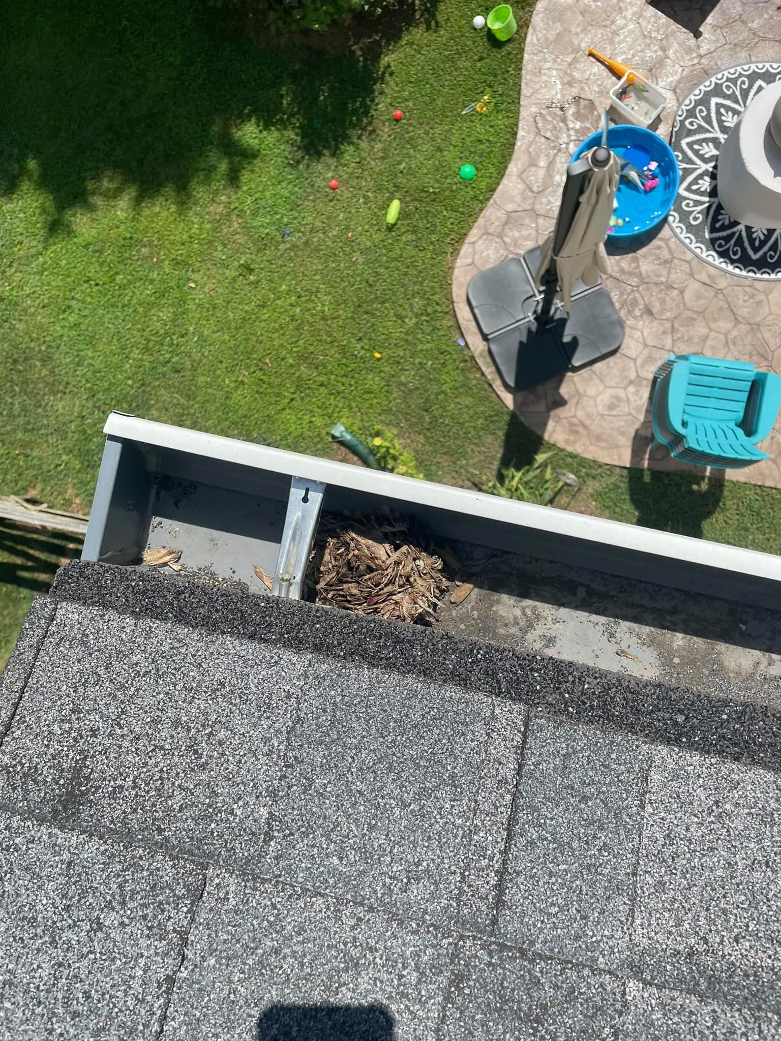 Backyard seen from above with lawn, patio chairs, a blue bucket, and a rooftop edge with gravel.