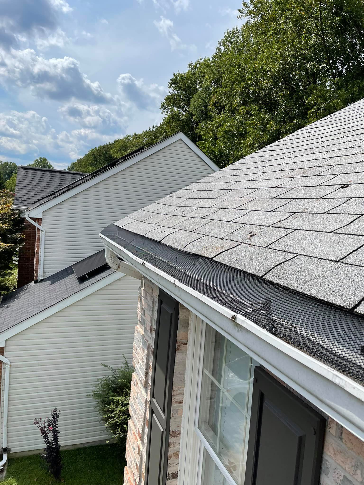 Rooftops with gray shingles beside white siding under a partly cloudy sky