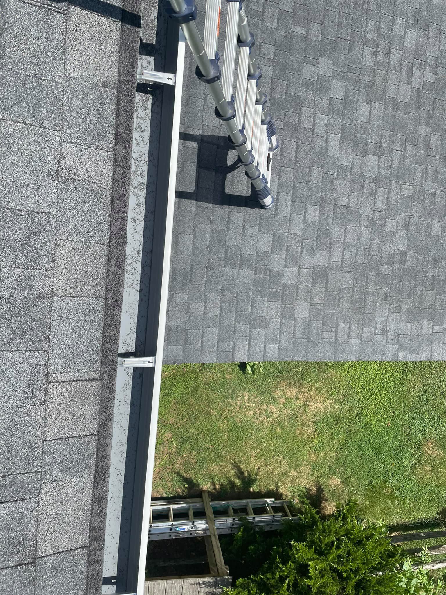 Rooftop gutter and downspout beside gray shingle roof and a patch of grass below.