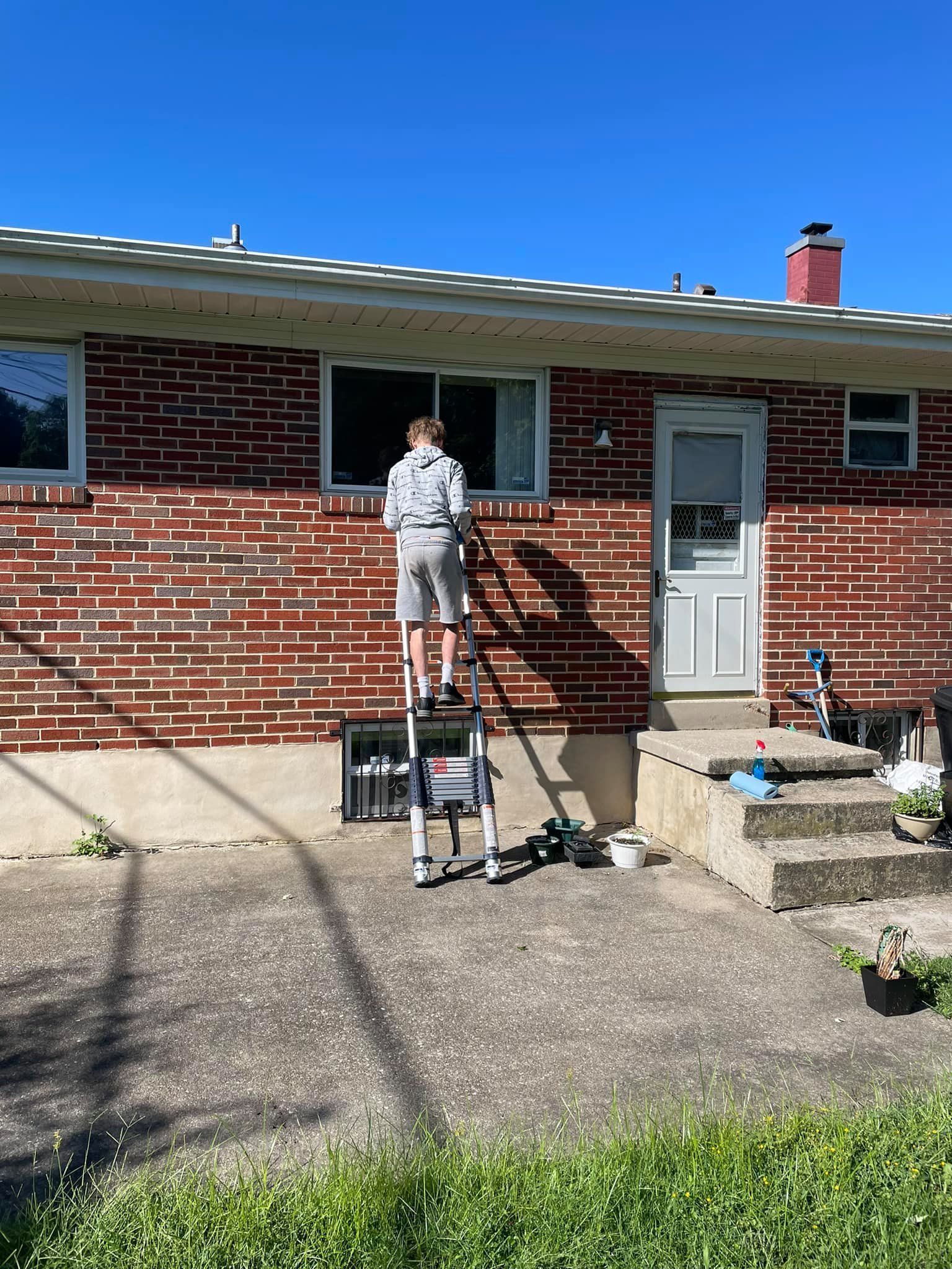 Person standing on a ladder painting a brick house exterior in sunlight