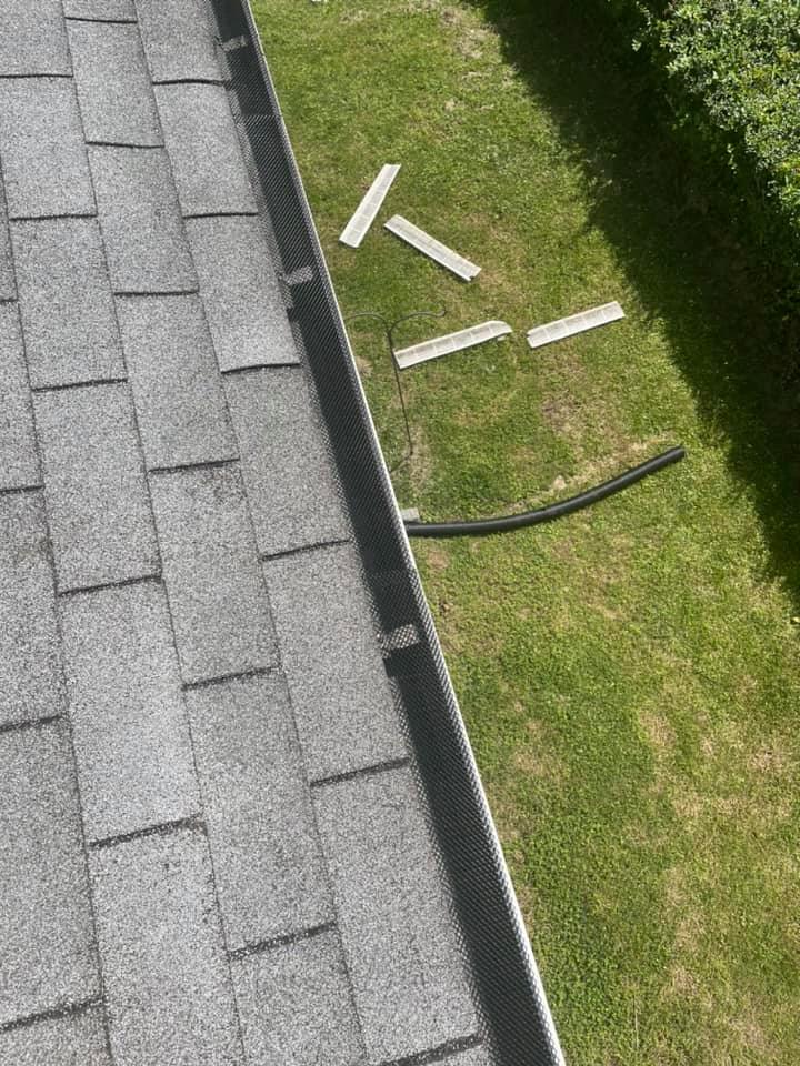 Roof gutter beside a grassy lawn with scattered white sticks and a black hose