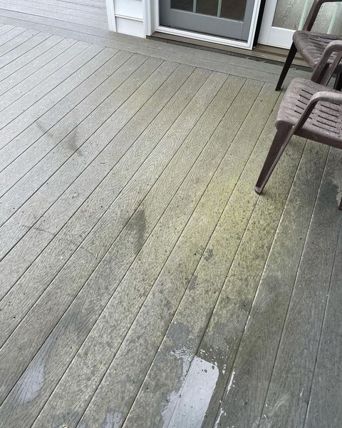 Weathered gray wooden deck with a small wet patch and chair legs near a sliding glass door