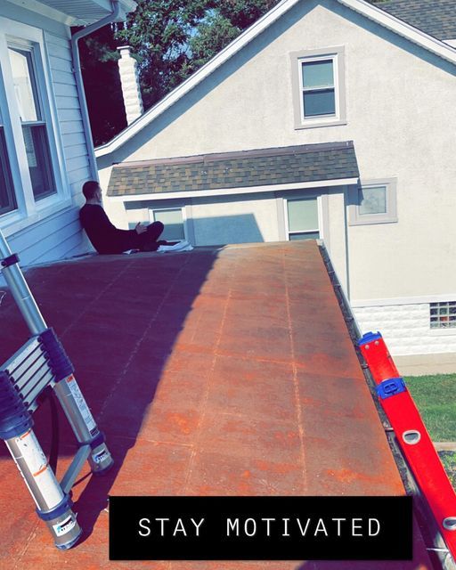Person sitting on a roof beside a ladder, with a red ladder and house exterior in the background.