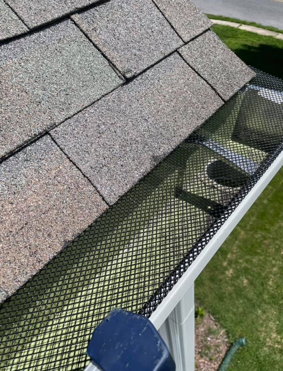 Close-up of a rain gutter with black leaf guard along a roof edge in autumn sunlight