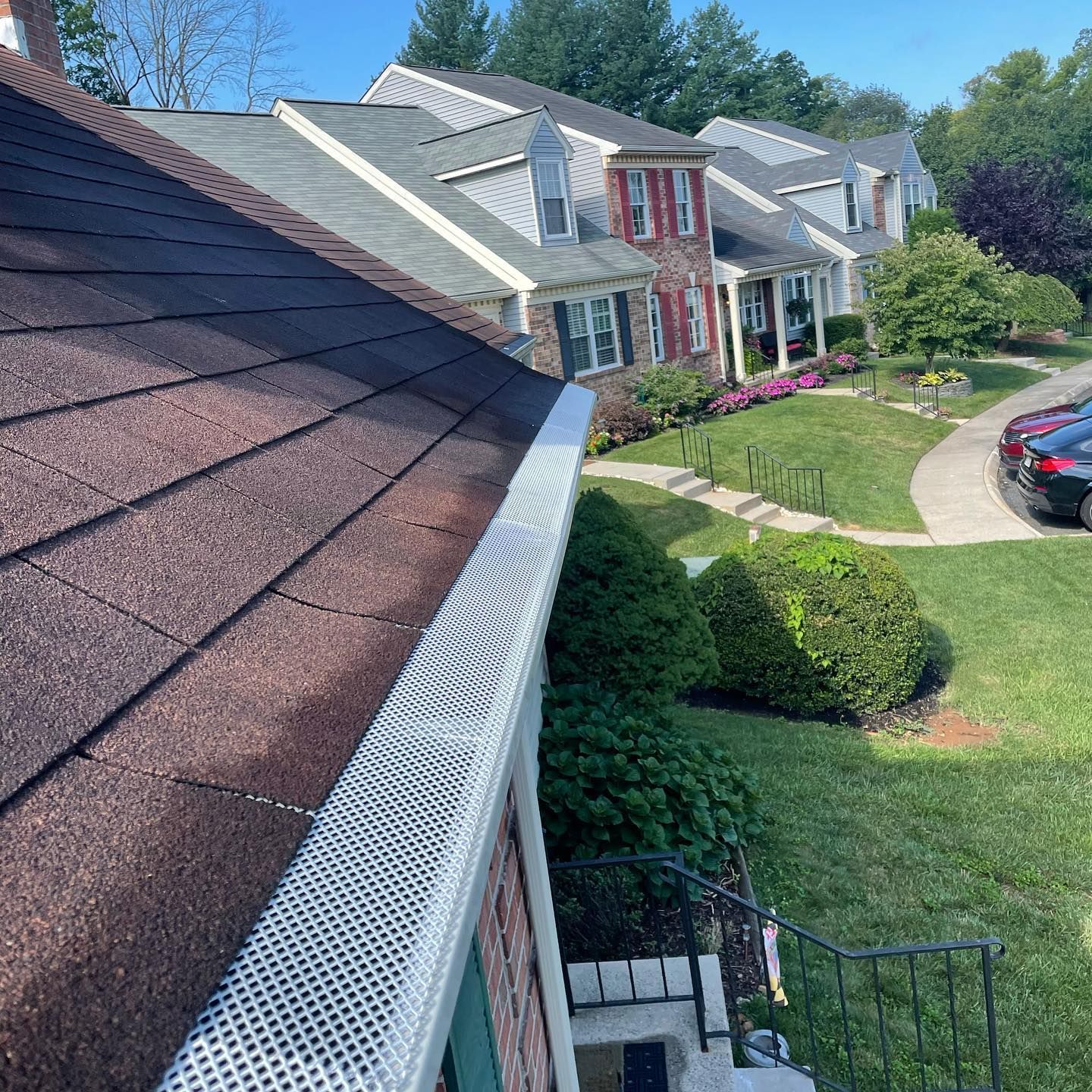 Roofline view of a suburban house with white gutter guards, green lawn, and a parked car on a sunny day