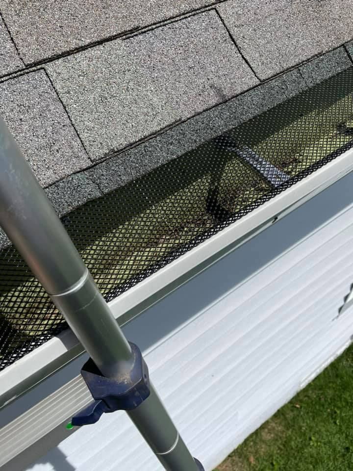 White siding and roof edge with a black gutter guard, seen beside a vertical metal pole and grass.