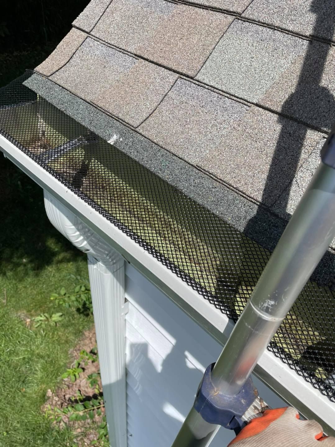 Gutter guard along a shingled roof edge beside a downspout and ladder rail
