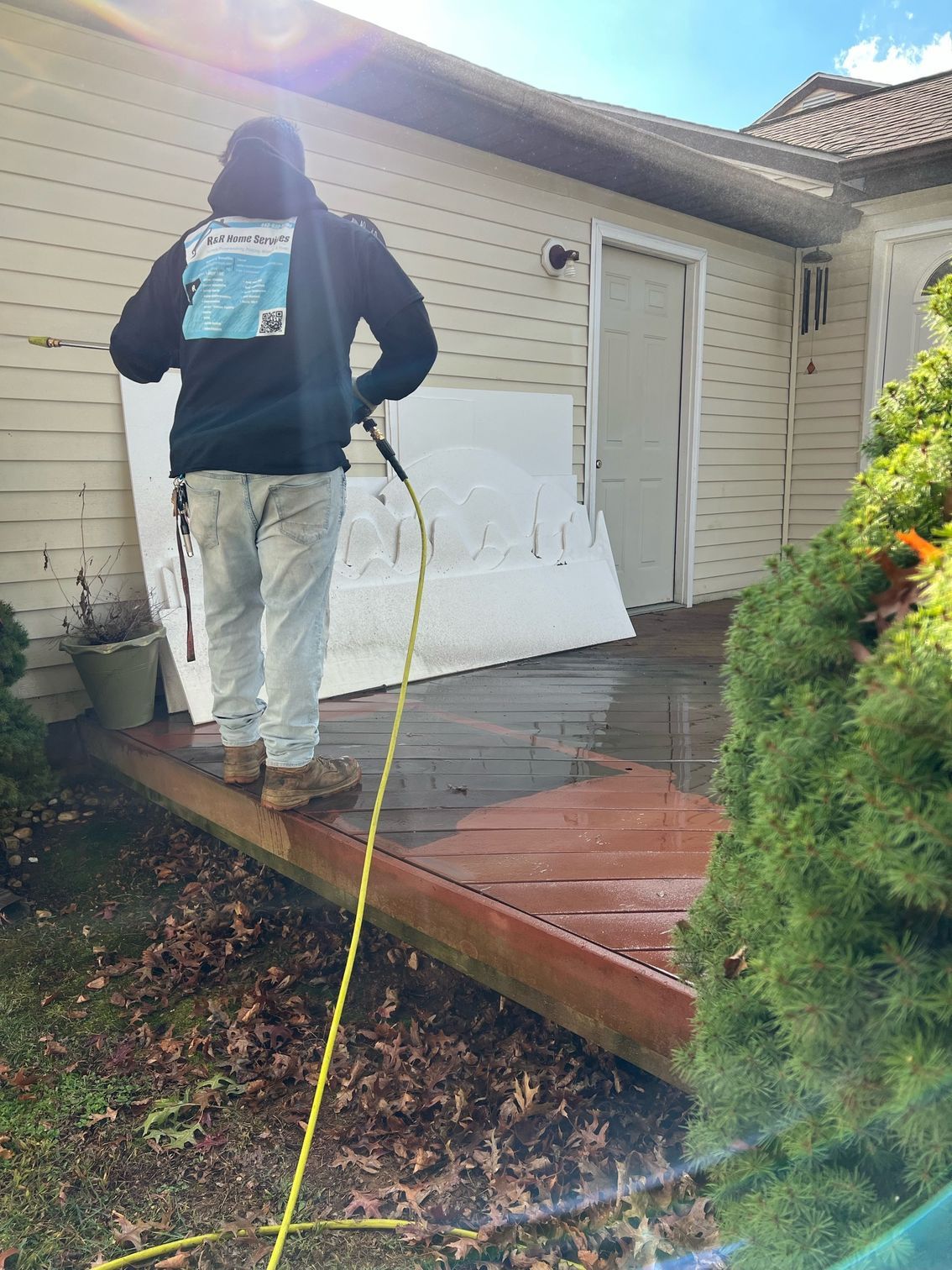 Person pressure washes a house porch beside a white door and shrubs.