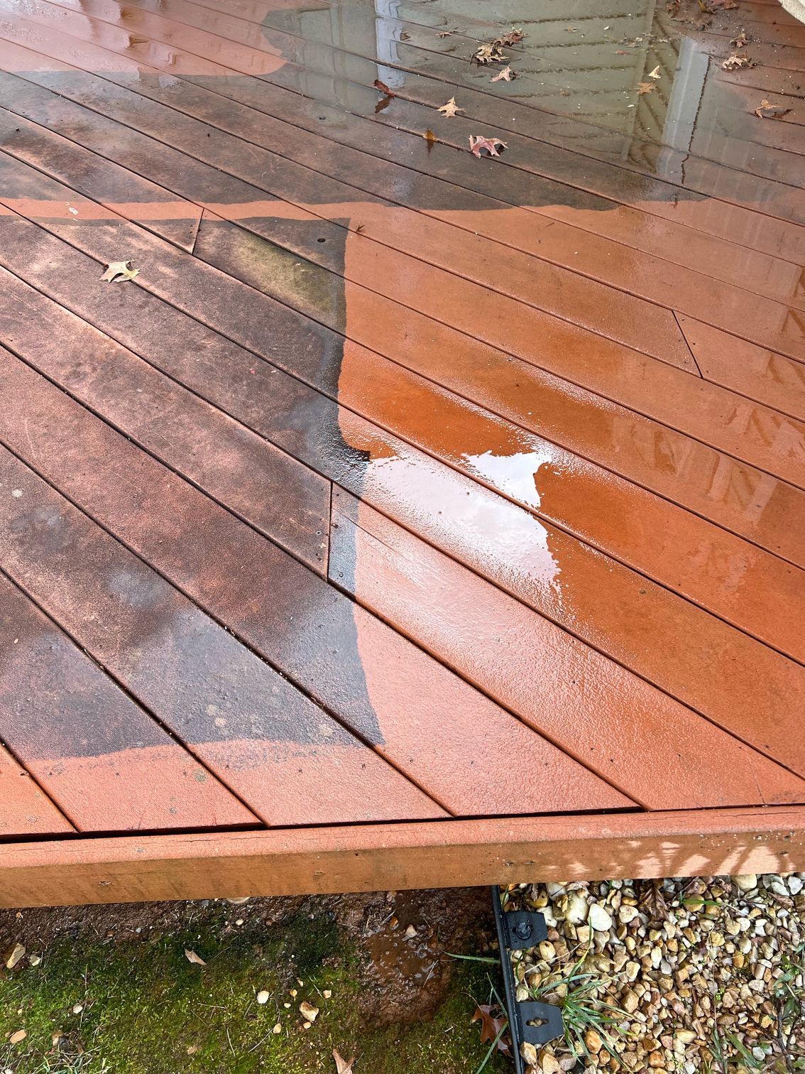 Wet wooden deck with a reflective puddle and scattered leaves near a gravel edge