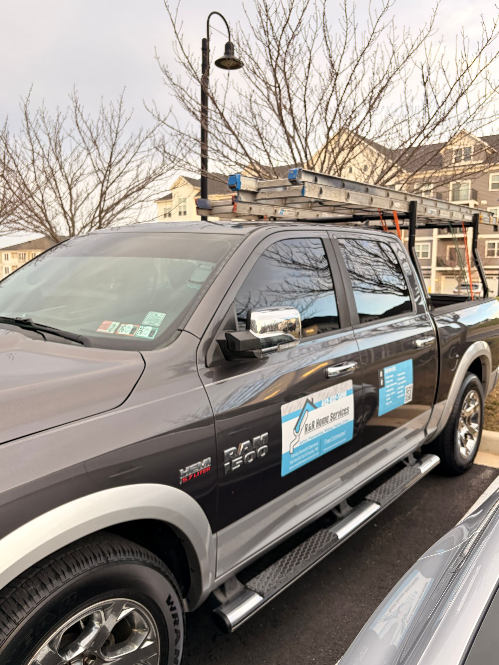 Black work pickup truck with ladders and signs parked on a street in a residential area