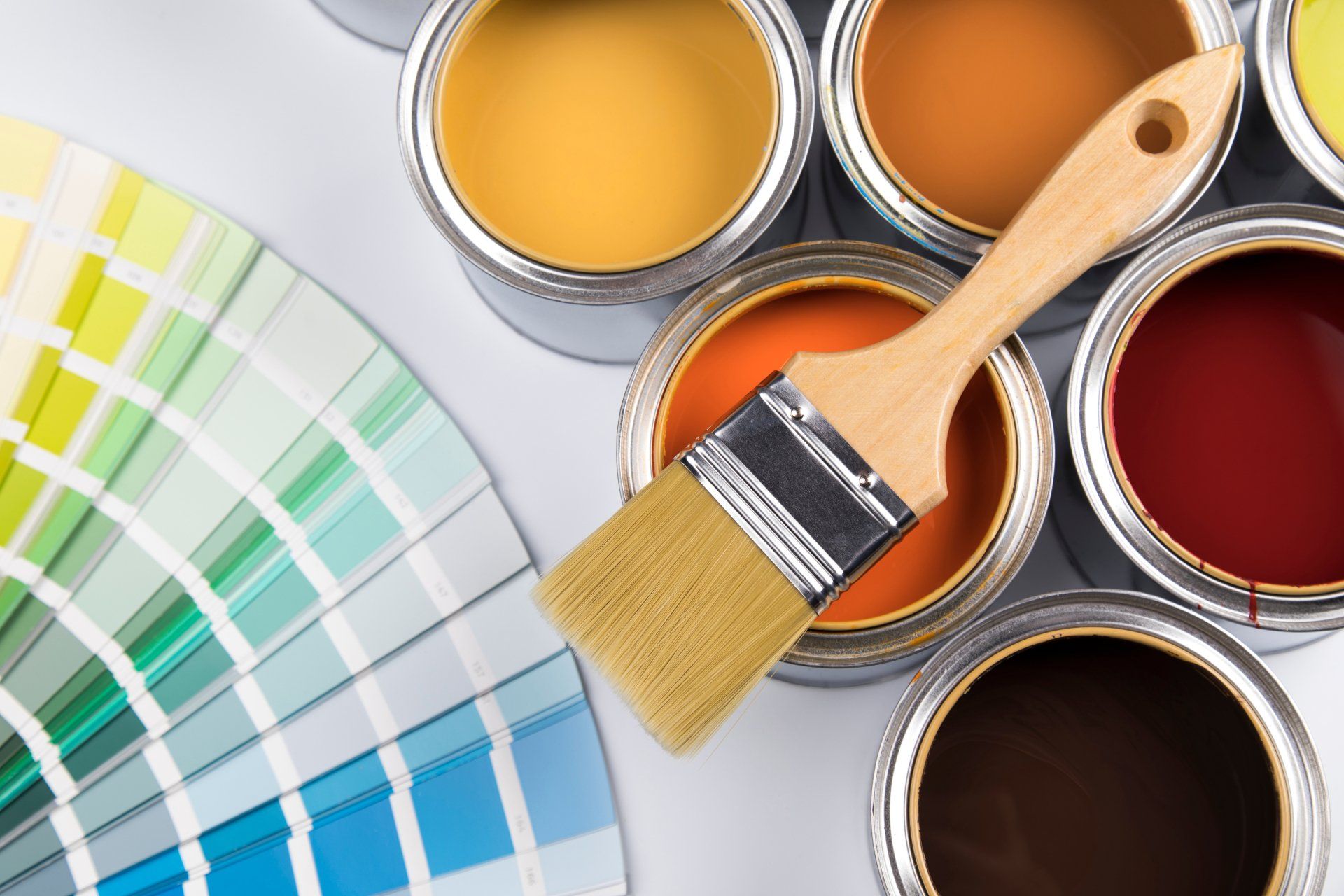 Paint brush resting on open paint cans beside a color swatch fan and palette of bright colors