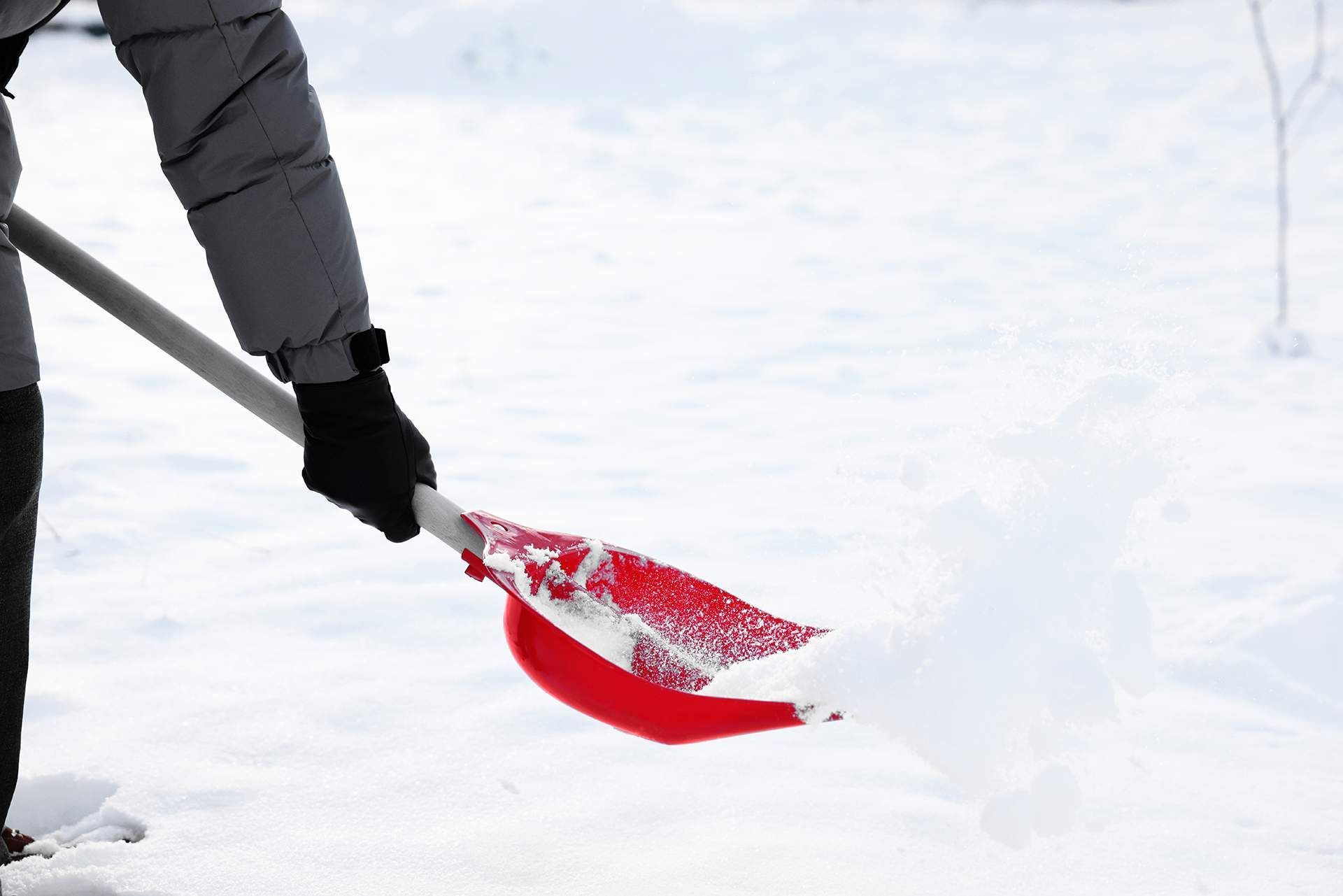 Person shoveling snow with a red snow shovel on a snowy ground