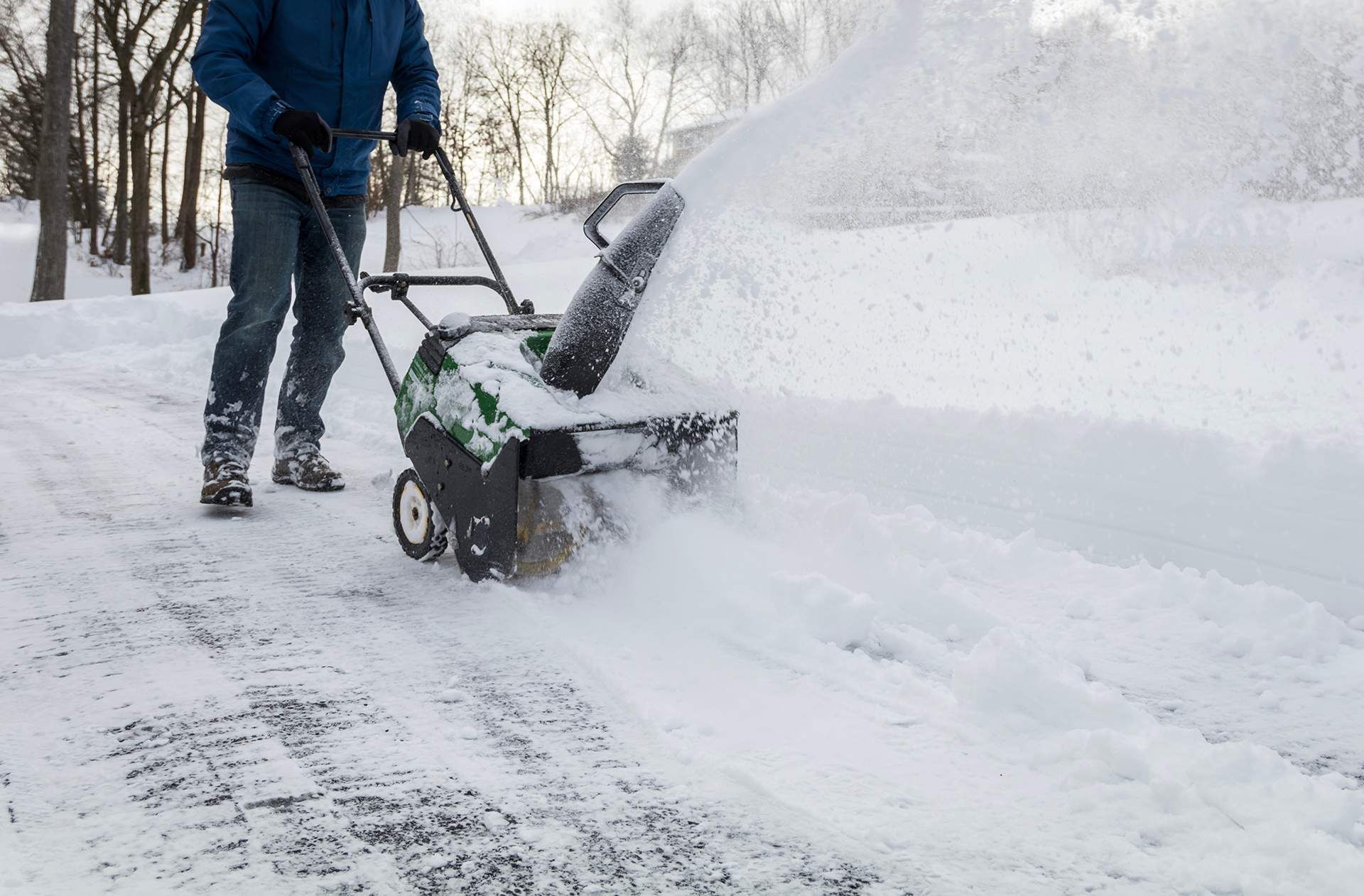 Person using a snowblower to clear a snowy driveway during heavy snowfall