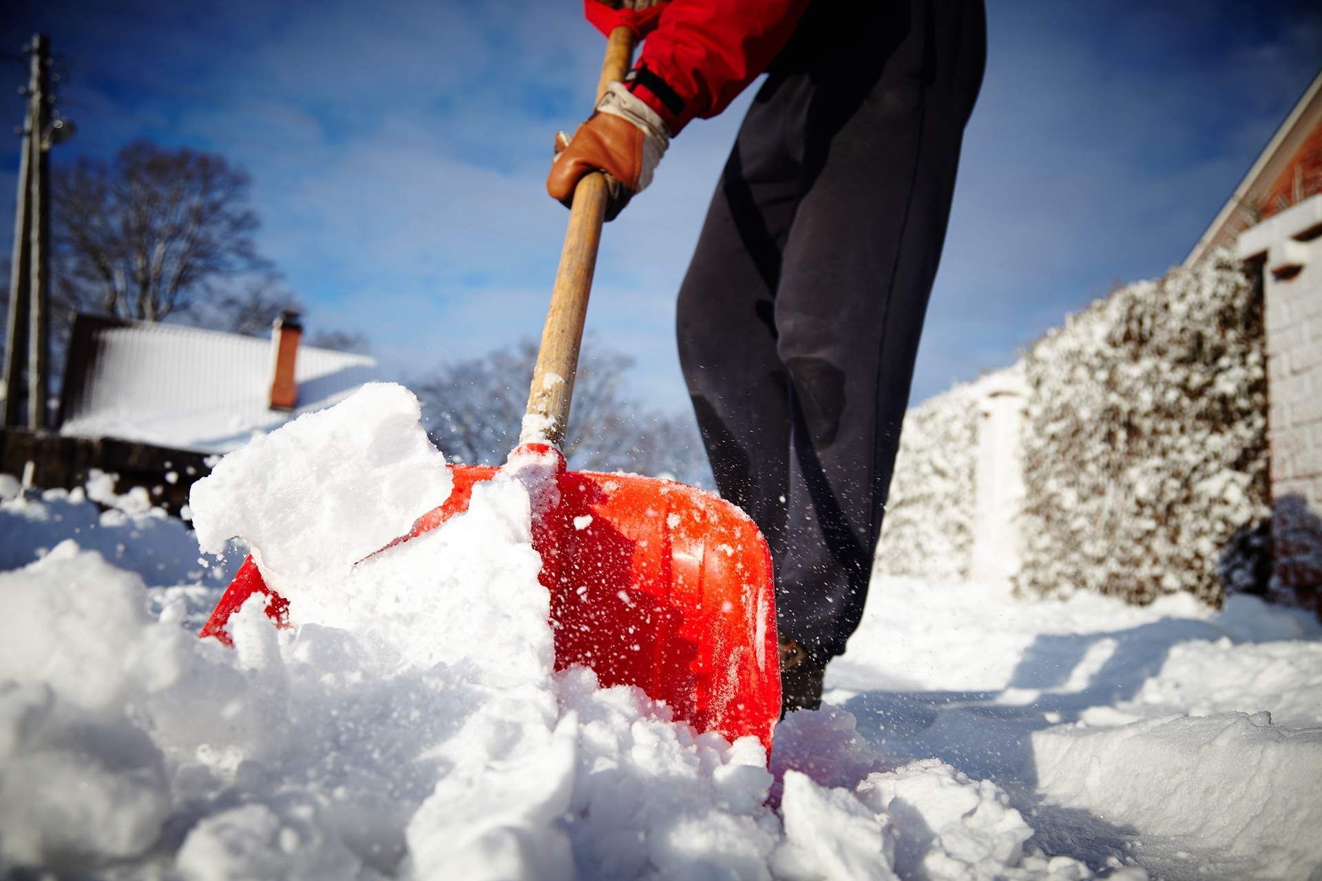 Person shoveling snow outdoors with a red shovel in a snowy yard