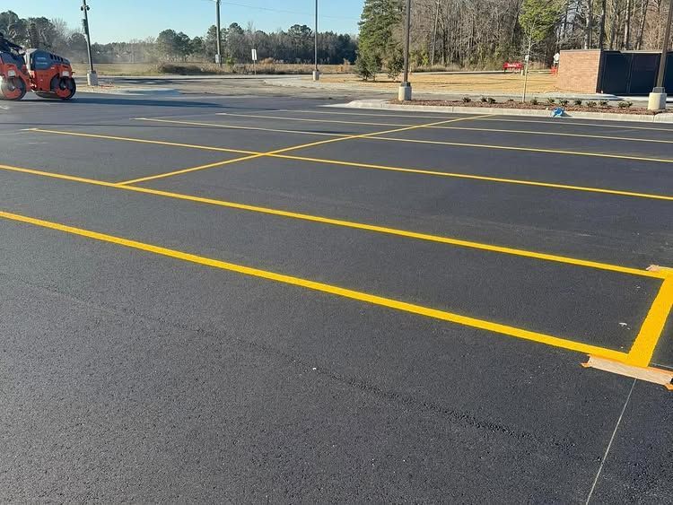 Empty asphalt parking lot with bright yellow painted lines and a red vehicle at the far left.