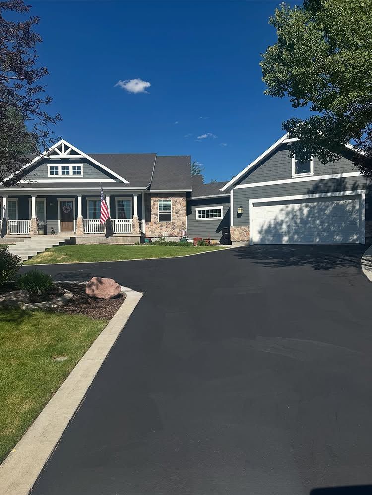 Suburban house with stone facade, attached garage, and black driveway under a clear blue sky