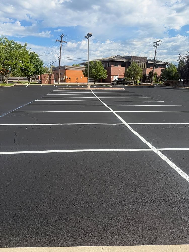 Empty parking lot with fresh white lines beside brick buildings and trees under a blue sky