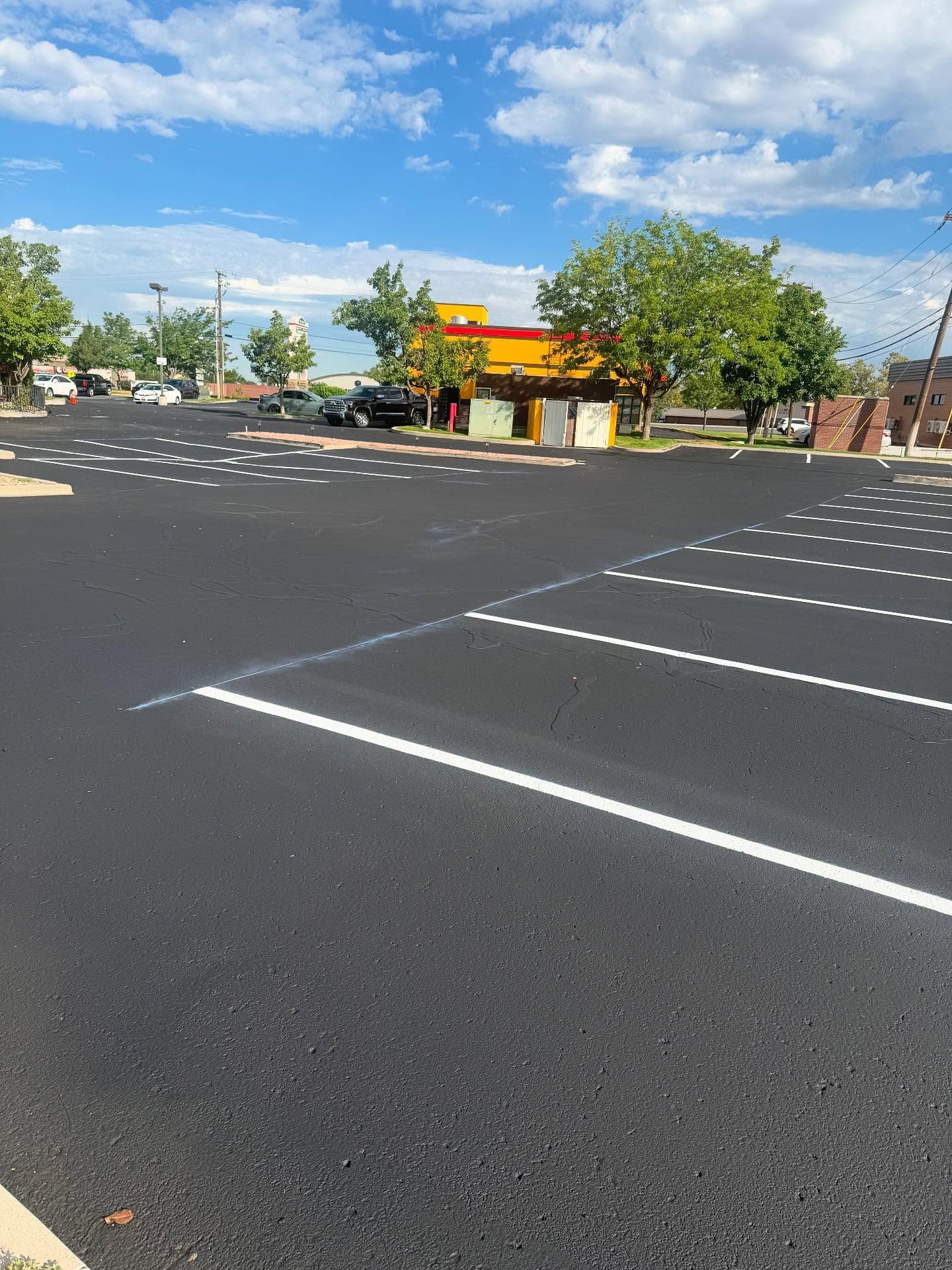 Empty parking lot with white lines, a yellow building, trees, and blue sky with clouds
