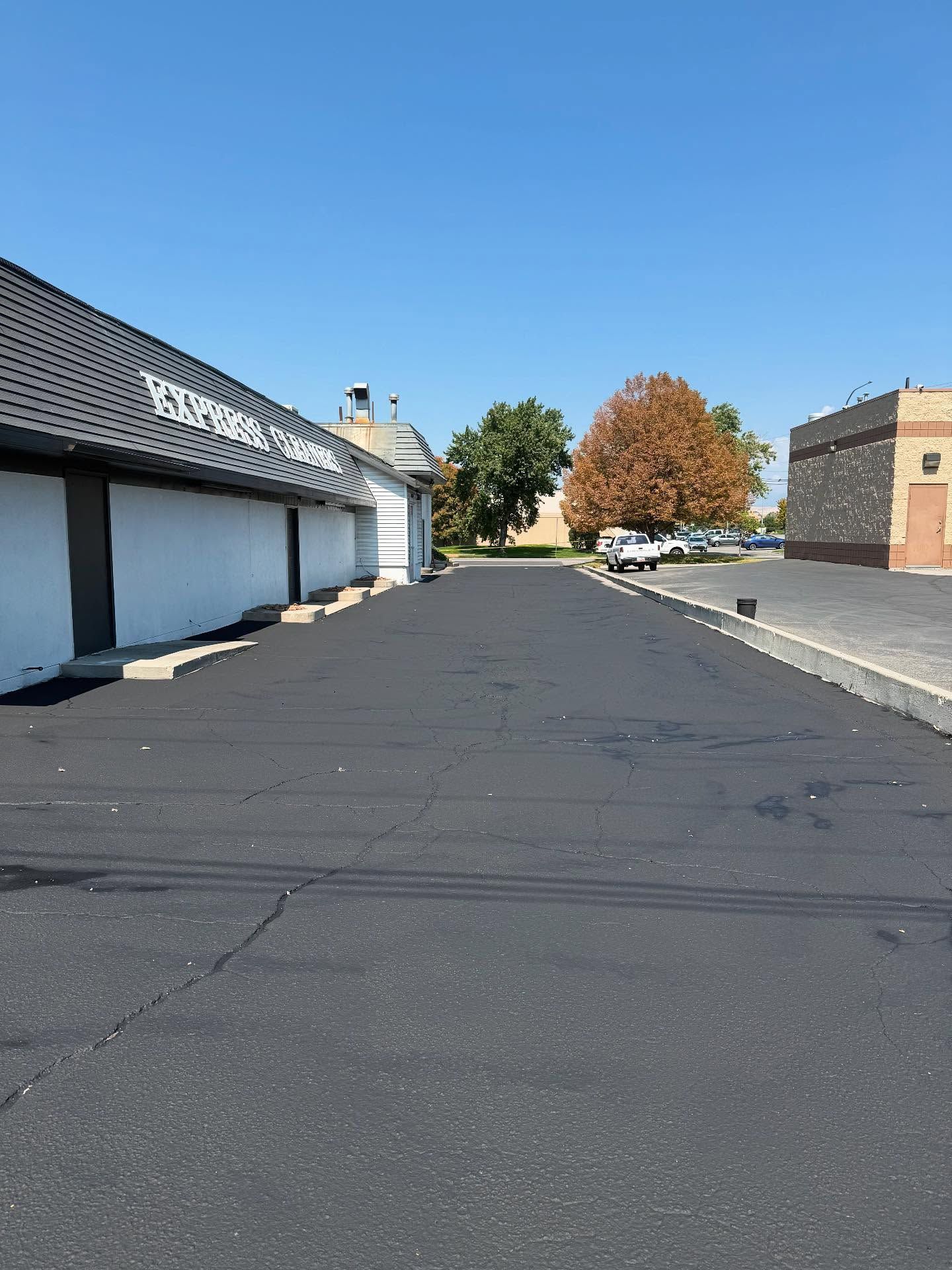 Empty parking lot beside white building under a clear blue sky with a tree in autumn colors.